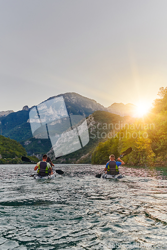 Image of A group of friends enjoying fun and kayaking exploring the calm river, surrounding forest and large natural river canyons during an idyllic sunset.