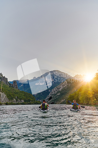 Image of A group of friends enjoying fun and kayaking exploring the calm river, surrounding forest and large natural river canyons during an idyllic sunset.