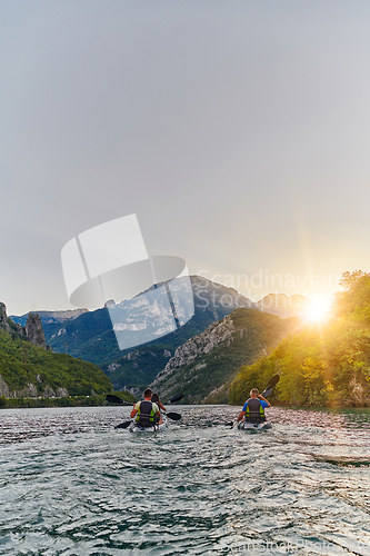 Image of A group of friends enjoying fun and kayaking exploring the calm river, surrounding forest and large natural river canyons during an idyllic sunset.