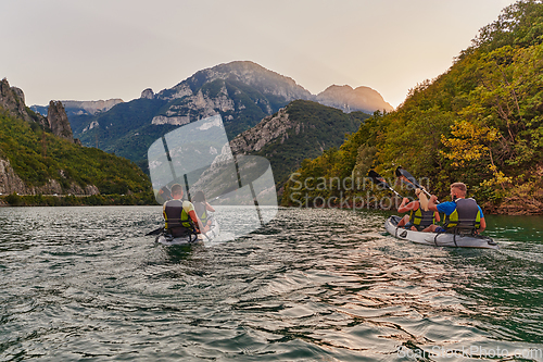 Image of A group of friends enjoying fun and kayaking exploring the calm river, surrounding forest and large natural river canyons during an idyllic sunset.