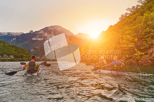 Image of A group of friends enjoying fun and kayaking exploring the calm river, surrounding forest and large natural river canyons during an idyllic sunset.