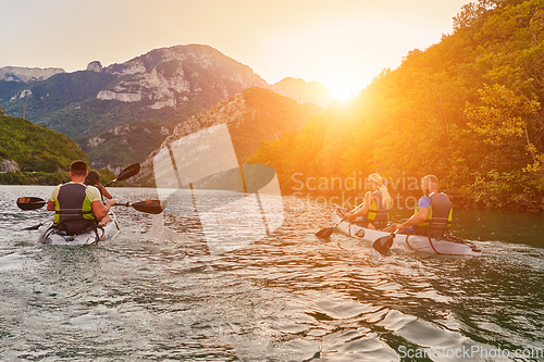 Image of A group of friends enjoying fun and kayaking exploring the calm river, surrounding forest and large natural river canyons during an idyllic sunset.