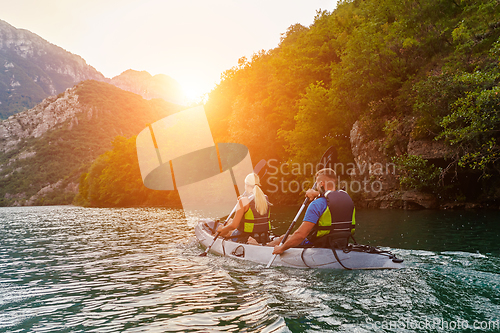 Image of A group of friends enjoying fun and kayaking exploring the calm river, surrounding forest and large natural river canyons during an idyllic sunset.