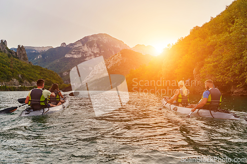 Image of A group of friends enjoying fun and kayaking exploring the calm river, surrounding forest and large natural river canyons during an idyllic sunset.