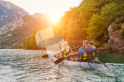 Image of A group of friends enjoying fun and kayaking exploring the calm river, surrounding forest and large natural river canyons during an idyllic sunset.