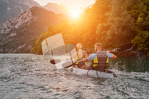 Image of A group of friends enjoying fun and kayaking exploring the calm river, surrounding forest and large natural river canyons during an idyllic sunset.