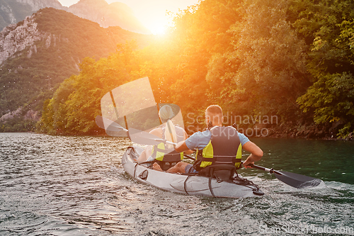 Image of A group of friends enjoying fun and kayaking exploring the calm river, surrounding forest and large natural river canyons during an idyllic sunset.