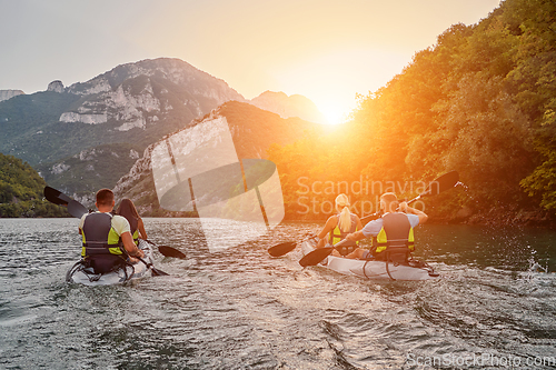 Image of A group of friends enjoying fun and kayaking exploring the calm river, surrounding forest and large natural river canyons during an idyllic sunset.