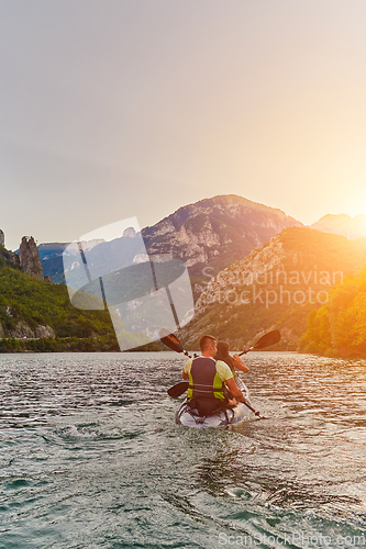 Image of A young couple enjoying an idyllic kayak ride in the middle of a beautiful river surrounded by forest greenery in sunset time