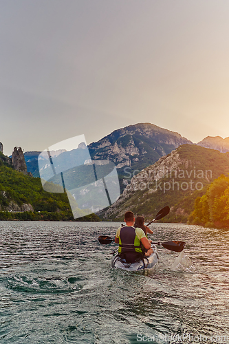 Image of A young couple enjoying an idyllic kayak ride in the middle of a beautiful river surrounded by forest greenery in sunset time