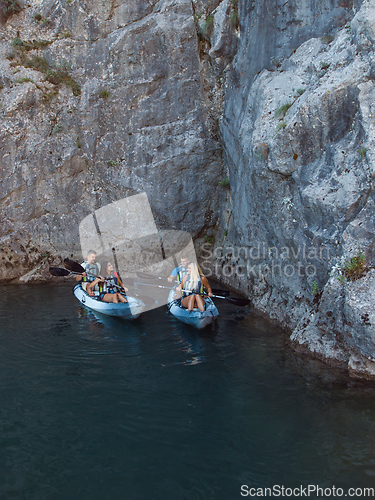 Image of A group of friends enjoying fun and kayaking exploring the calm river, surrounding forest and large natural river canyons during an idyllic sunset.