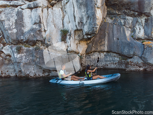 Image of A young couple enjoying an idyllic kayak ride in the middle of a beautiful river surrounded by forest greenery