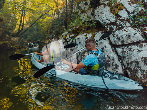 Image of A young couple enjoying an idyllic kayak ride in the middle of a beautiful river surrounded by forest greenery