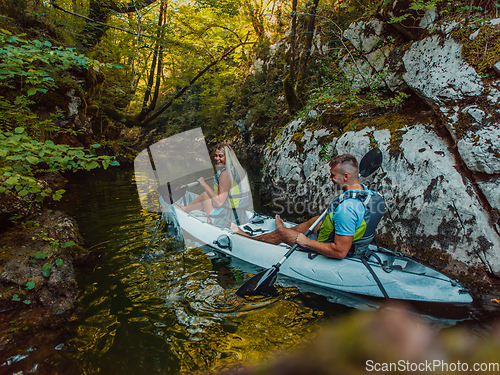 Image of A young couple enjoying an idyllic kayak ride in the middle of a beautiful river surrounded by forest greenery