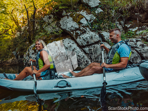 Image of A young couple enjoying an idyllic kayak ride in the middle of a beautiful river surrounded by forest greenery