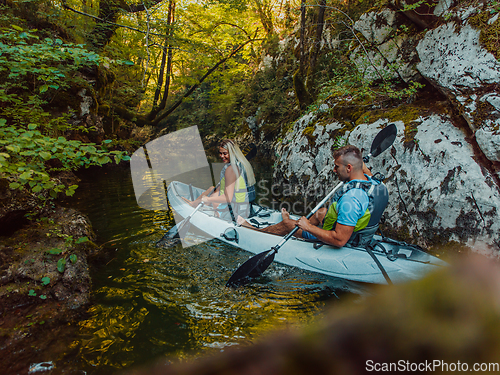 Image of A young couple enjoying an idyllic kayak ride in the middle of a beautiful river surrounded by forest greenery