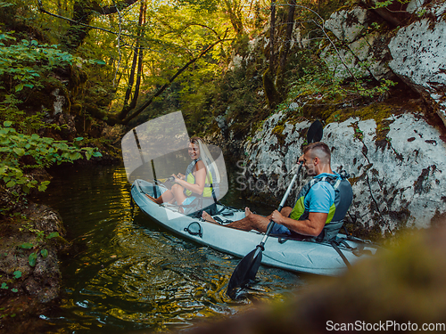 Image of A young couple enjoying an idyllic kayak ride in the middle of a beautiful river surrounded by forest greenery