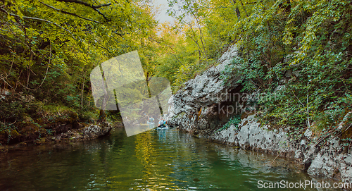 Image of A group of friends enjoying having fun and kayaking while exploring the calm river, surrounding forest and large natural river canyons