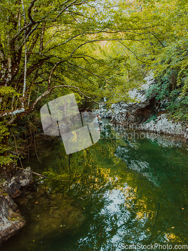 Image of A group of friends enjoying having fun and kayaking while exploring the calm river, surrounding forest and large natural river canyons