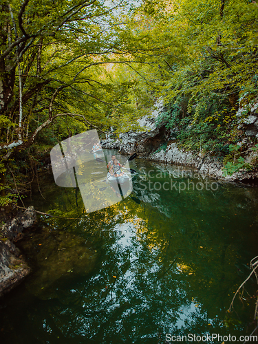 Image of A group of friends enjoying having fun and kayaking while exploring the calm river, surrounding forest and large natural river canyons