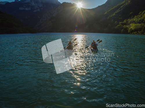 Image of A group of friends enjoying fun and kayaking exploring the calm river, surrounding forest and large natural river canyons during an idyllic sunset.