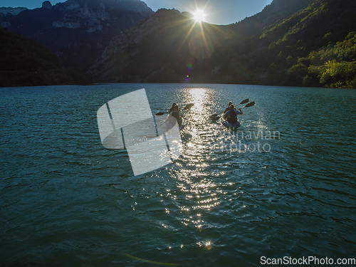 Image of A group of friends enjoying fun and kayaking exploring the calm river, surrounding forest and large natural river canyons during an idyllic sunset.