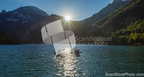 Image of A group of friends enjoying fun and kayaking exploring the calm river, surrounding forest and large natural river canyons during an idyllic sunset.