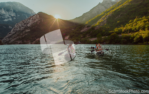 Image of A group of friends enjoying fun and kayaking exploring the calm river, surrounding forest and large natural river canyons during an idyllic sunset.