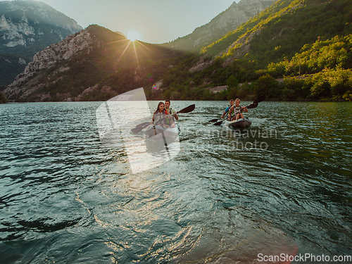 Image of A group of friends enjoying fun and kayaking exploring the calm river, surrounding forest and large natural river canyons during an idyllic sunset.