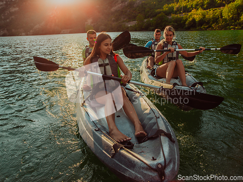 Image of A group of friends enjoying fun and kayaking exploring the calm river, surrounding forest and large natural river canyons during an idyllic sunset.