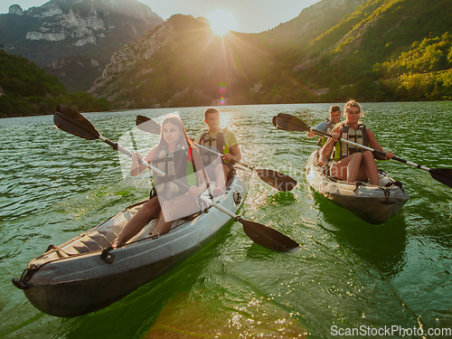 Image of A group of friends enjoying fun and kayaking exploring the calm river, surrounding forest and large natural river canyons during an idyllic sunset.