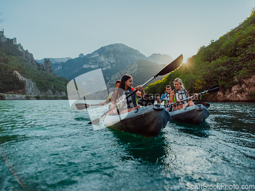 Image of A group of friends enjoying fun and kayaking exploring the calm river, surrounding forest and large natural river canyons during an idyllic sunset.