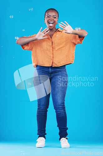 Image of Excited, portrait and black woman on blue background with bubbles for happiness, joy and have fun. Playful, smile and isolated African person in studio with soap bubble for happy, magic and aesthetic