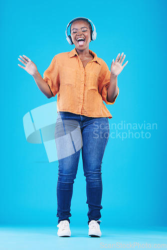 Image of Black woman, headphones and singing to music with dance in a studio. Audio streaming, radio and happy female person with blue background and excited from celebration and freedom with hip hop song