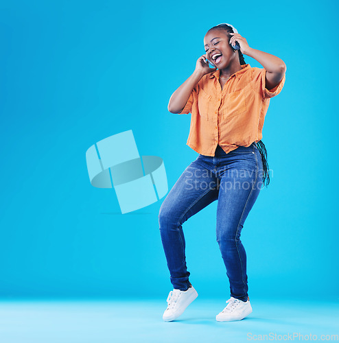 Image of Black woman, headphones and dancing to music with singing in a studio. Audio streaming, radio and happy female person with blue background and excited from celebration and freedom with hip hop song