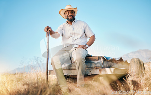 Image of Happy, African farmer and portrait in the countryside and man, sitting and watching over environment, field and land. Farming, meadow and agriculture worker outdoor with smile or happiness in summer