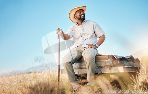 Image of Happy, African farmer and land in the countryside and man, sitting and watching over agriculture, field and environment. Farming, meadow and worker outdoor with smile in summer with happiness