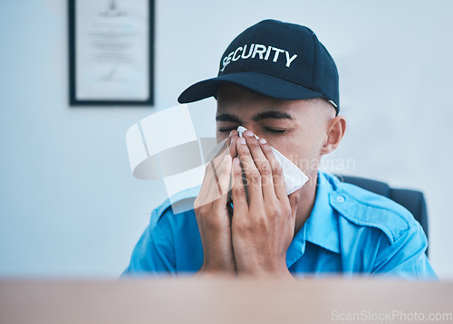 Image of Man, blowing nose and working at desk in office for security, safety or surveillance control room or person with allergies or hayfever. Sick, guard and employee with flu, virus or tissue for sneeze