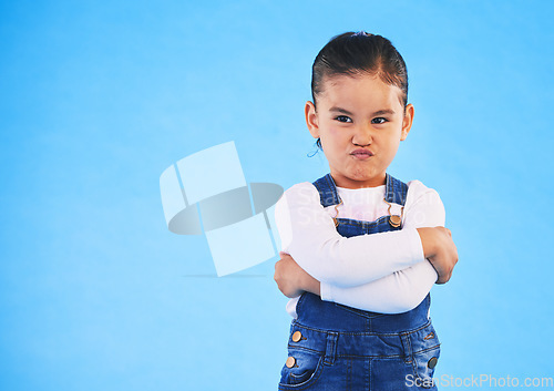 Image of Angry, child and arms crossed with tantrum in studio with mockup space. Kid, young girl and frustrated with cross frown and pout with a problem and mad attitude with blue background and grumpy