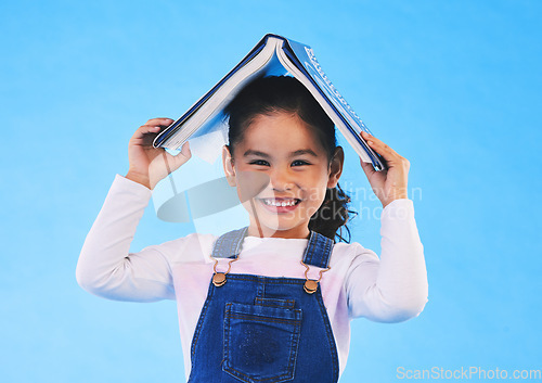 Image of School, head and portrait of kid with book for knowledge or learning isolated in a studio blue background. Clever, smart and young girl child with notebook happy for education, story or reading