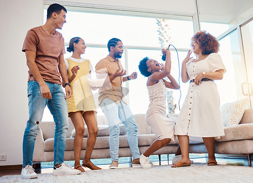 Image of Karaoke, entertainment and friends singing in the living room with a microphone to music, playlist or radio. Happy, diversity and young people dancing, bonding and having fun together at an apartment