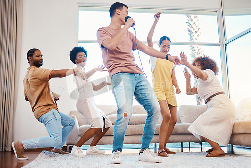 Image of Karaoke, group and friends singing in the living room with a microphone to music, playlist or radio. Happy, diversity and young people dancing, bonding and having fun together with a song at home.