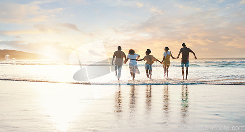 Image of Friends, holding hands and running to water on beach, sunset or vacation, holiday and summer break with freedom. Group, silhouette and people together in ocean, waves or sea with support in community