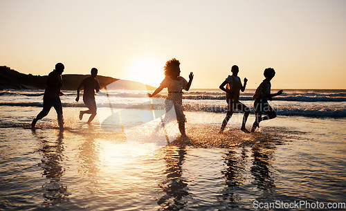 Image of Sunset, beach and friends with freedom, running and having fun in water together on summer vacation. Ocean, silhouette and group of people at the sea for holiday, bond and travel celebration in Bali