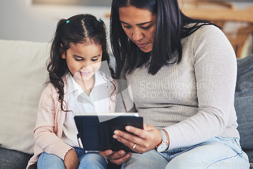 Image of Tablet, education and a mother on the sofa with her daughter in the living room of their home together. School, family or children with a mother and girl looking at an online homework assignment