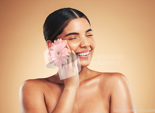 Image of Skincare, smile and woman with flower in studio for beauty, wellness and organic cosmetics on brown background. Floral, dermatology and hand on face of model happy with plant, cosmetology or results