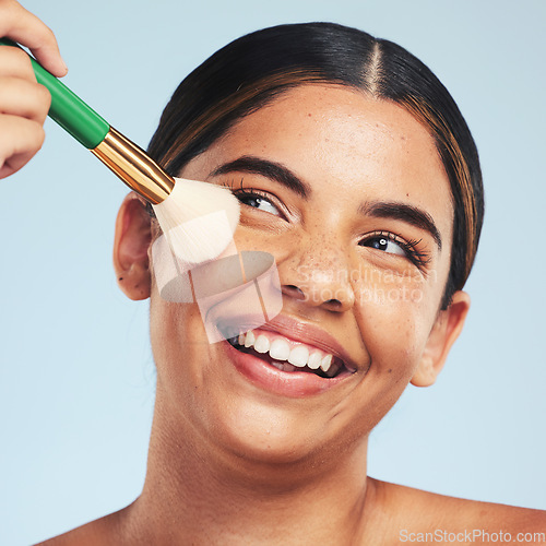 Image of Face, happy woman and brush for makeup in studio to apply foundation for glow on blue background. Model, smile and aesthetic cosmetics for skincare tools, facial beauty powder or thinking of makeover