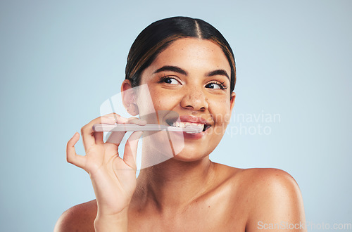 Image of Woman, happy and brushing teeth in studio for healthy dental wellness on blue background. Face of model thinking with toothbrush while cleaning mouth for fresh breath, oral hygiene or care of smile