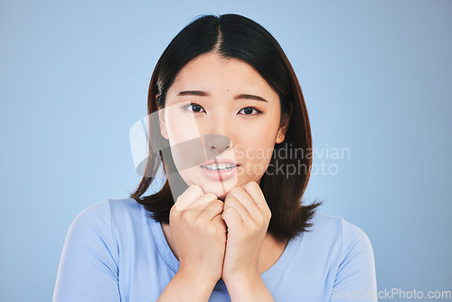 Image of Asian, portrait and scared woman with surprise from announcement, news or horror story on blue background in studio. Shock, face and person in danger with fear in facial expression, hands or reaction