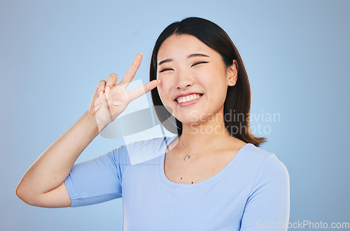 Image of Peace, sign and portrait of woman with hand for emoji in studio blue background with gen z style, fashion or happiness. Face, smile and Asian model with gesture, expression